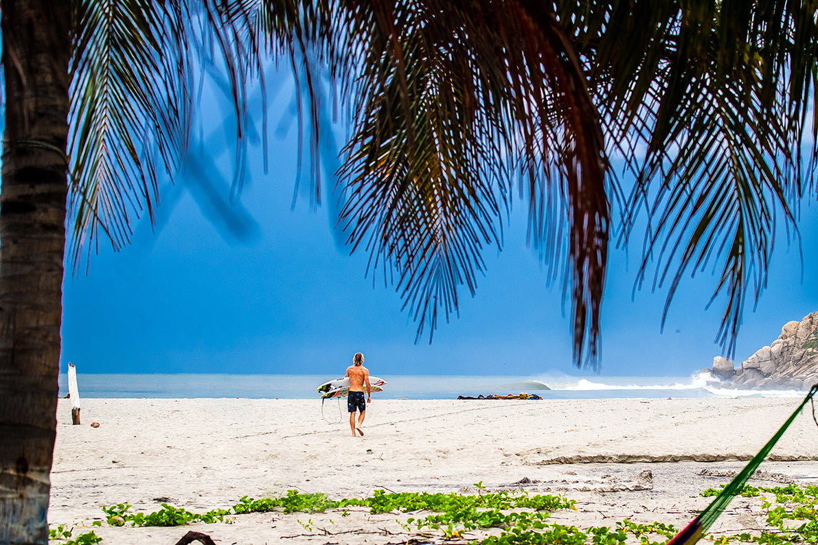 Beautiful warm beach landscape with a surfer walking on the sand