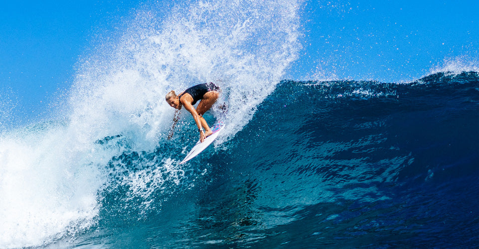 Surfer riding a large wave with blue sky in the background