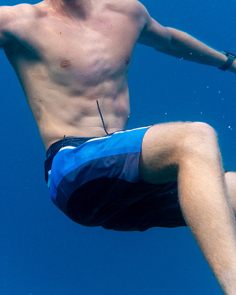 Person wearing blue swim shorts underwater with a clear blue background