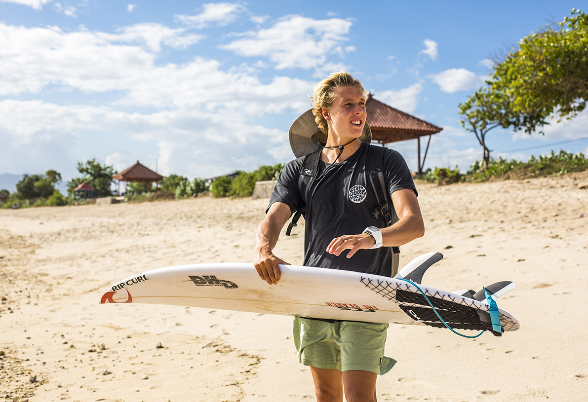 Jacob Willcox standing at the beach with his surfboard