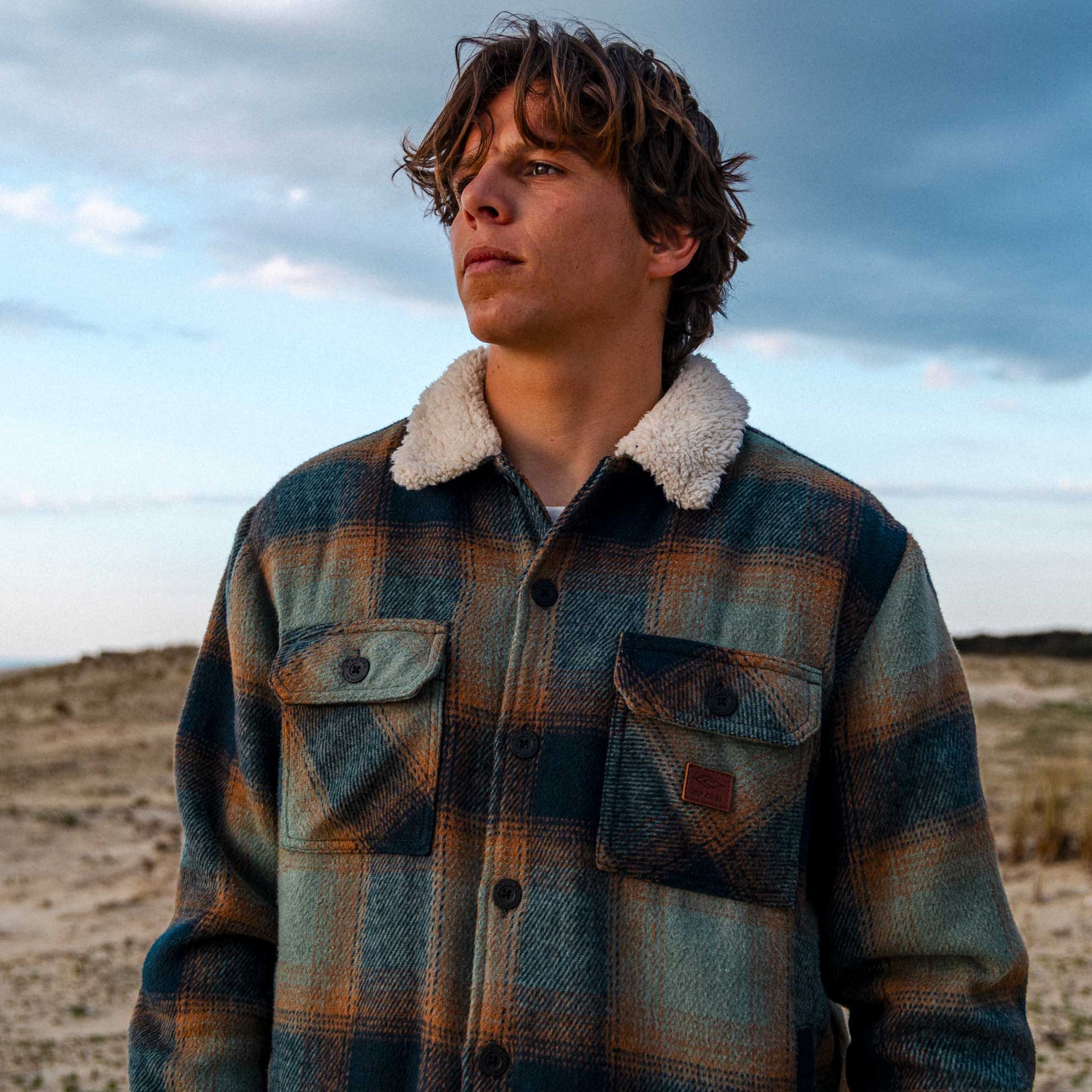 Person wearing a plaid shirt with a fur-lined collar in a desert setting