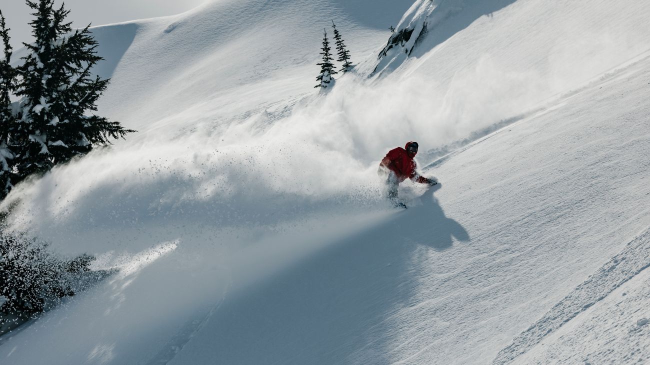 ici on voit le snowboardeur Chris Rasman en pleine action dans la poudreuse, il envoie une gerbe de neige derrière lui.