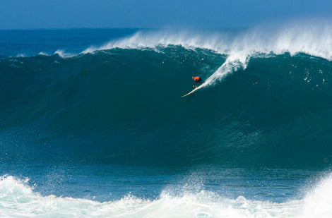 Surfer riding a large wave in the ocean with clear blue sky.