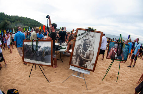 People gathered on a beach with portraits displayed on easels.
