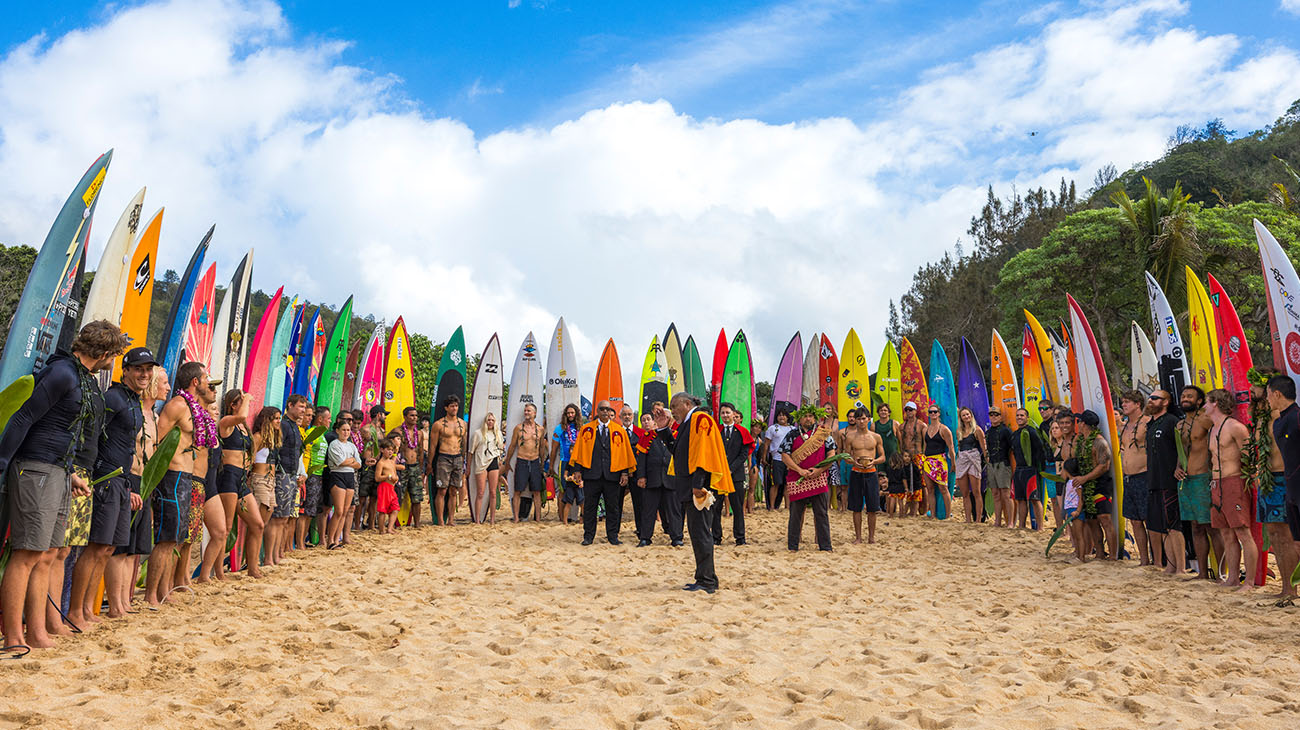 Group of people on a beach with colorful surfboards lined up against a blue sky.