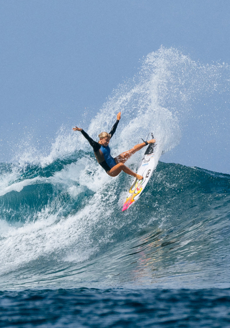 Surfer performing a trick on a wave with a clear blue sky
