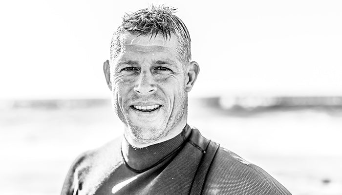 Black and white photo of Mick Fanning wearing a wetsuit with a blurred background
