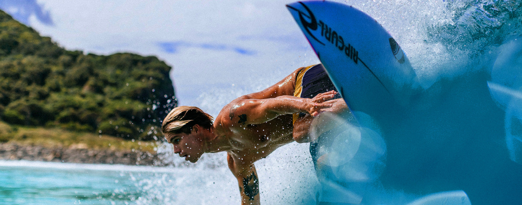 Surfer performing a trick on a wave with a clear blue sky and greenery in the background