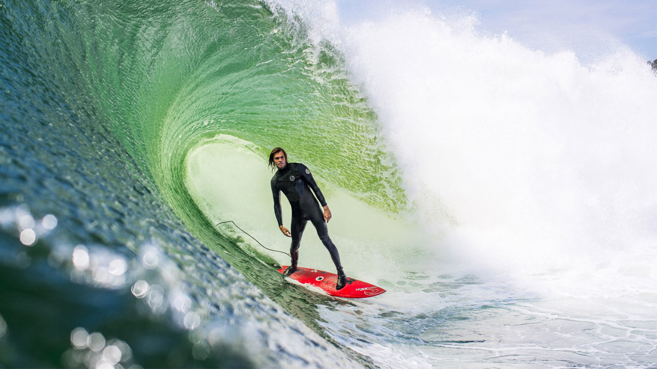 Surfer riding a wave in a black wetsuit on a red surfboard.