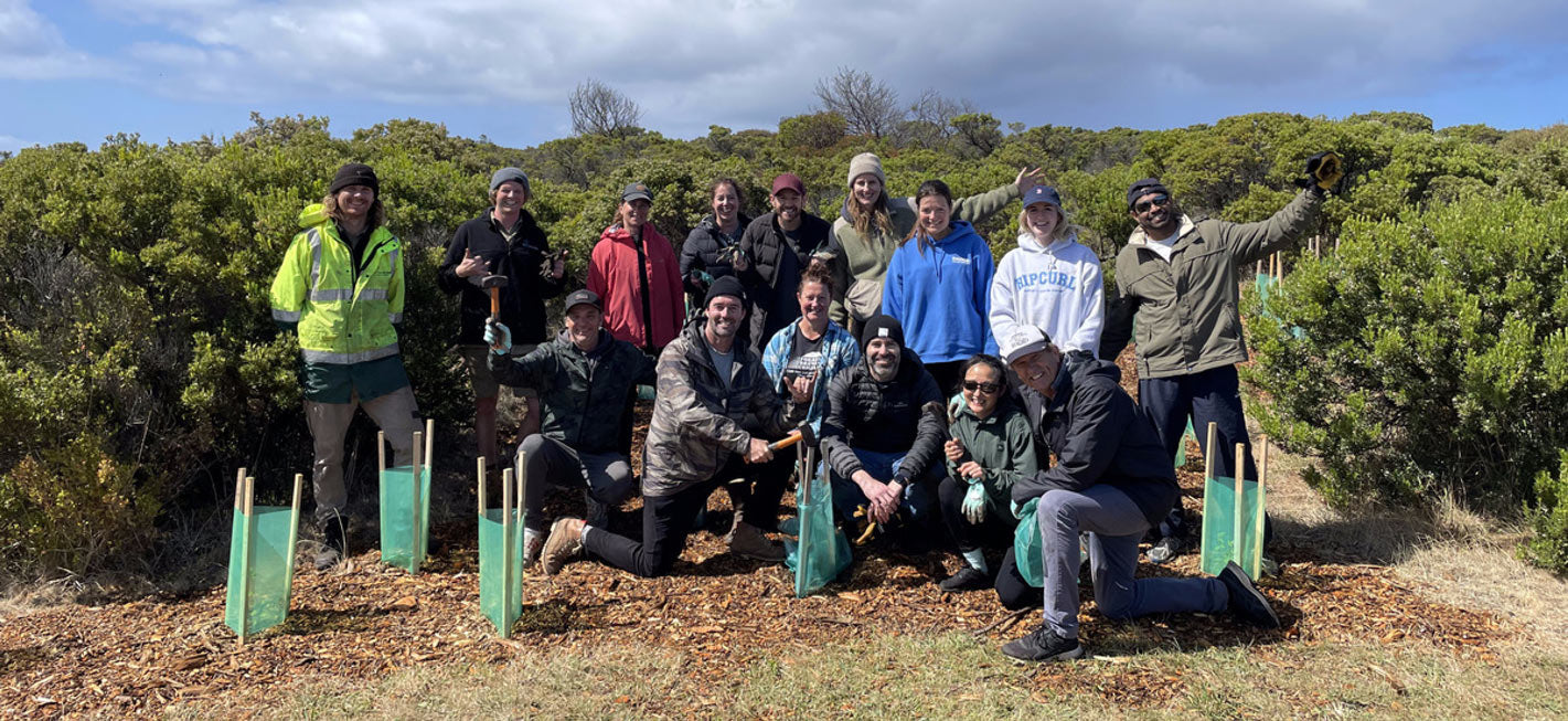 Group of people posing outdoors with green planters in a natural setting